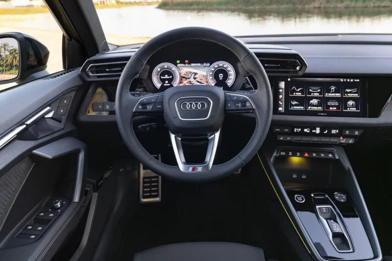 Audi A3 zakelijk leasen - stuurwiel en dashboard met S-embleem, zeezicht op de achtergrond