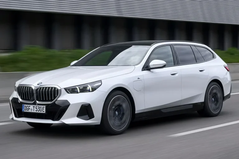 BMW 5-Serie Touring leasen - schuin vooraanzicht tijdens het rijden bij een industrieel gebouw