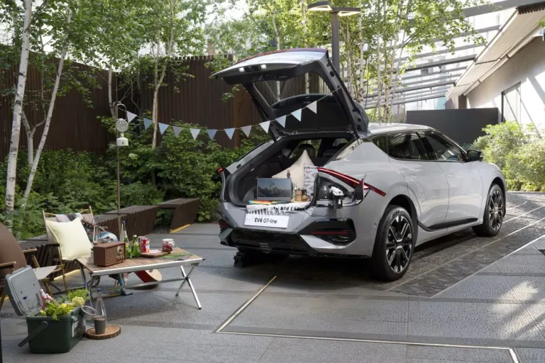 Kia EV6 leasen - schuin achteraanzicht met geopende achterklep in een tuin met picknickspullen