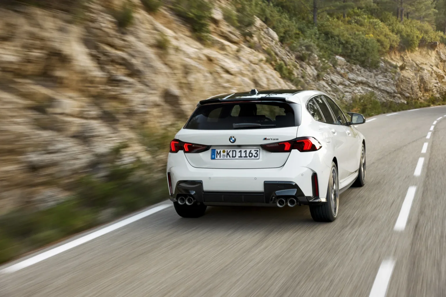 BMW 1-Serie leasen - schuin achteraanzicht van de rijdende witte hatchback op een bergweg