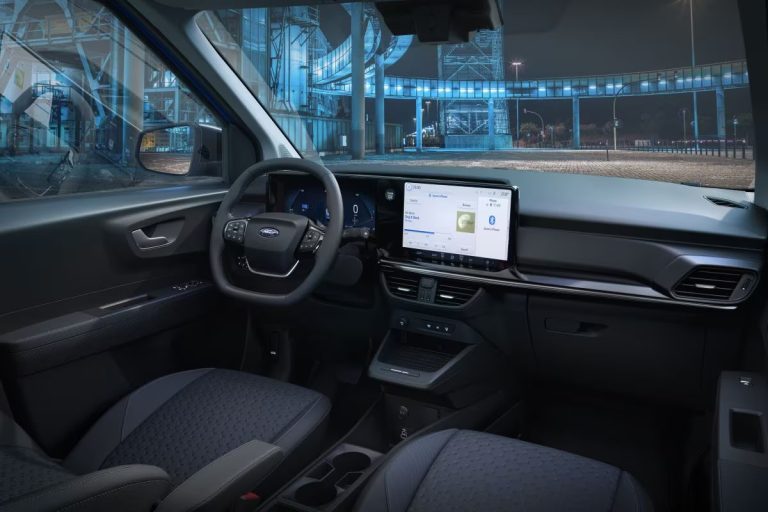 Ford Transit Courier leasen - interieur met stuurwiel en middenscherm, industriële omgeving op de achtergrond