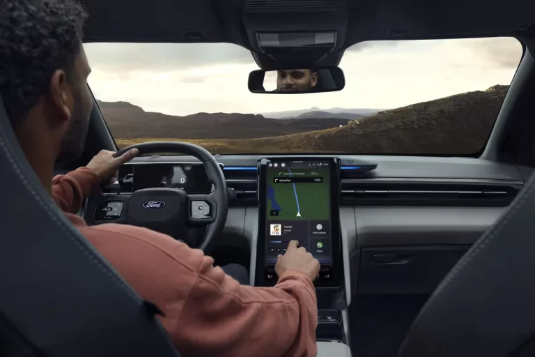 Ford Explorer BEV leasen - bestuurder bedient het touchscreen met navigatiekaart, berglandschap op de achtergrond