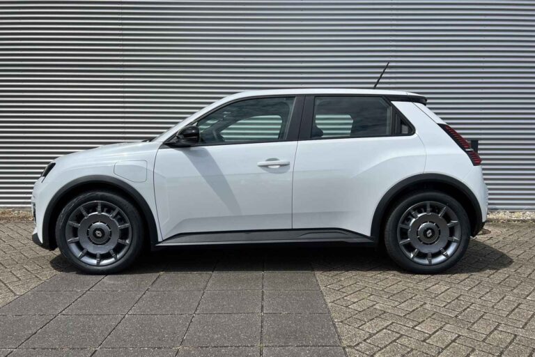 Renault 5 uit voorraad - zijaanzicht van de witte hatchback bij een gegolfde gevel