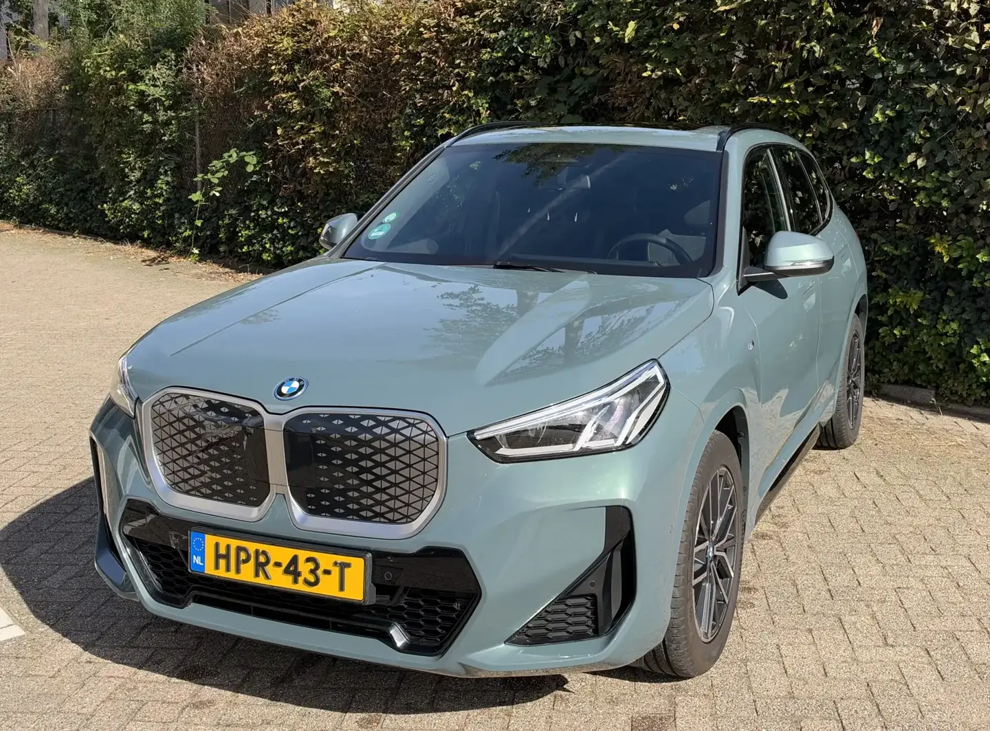 BMW iX1 occasion lease, Cape York Green iX1 eDrive20 M Sport schuin van voren links met M-bumper en 18-inch velgen