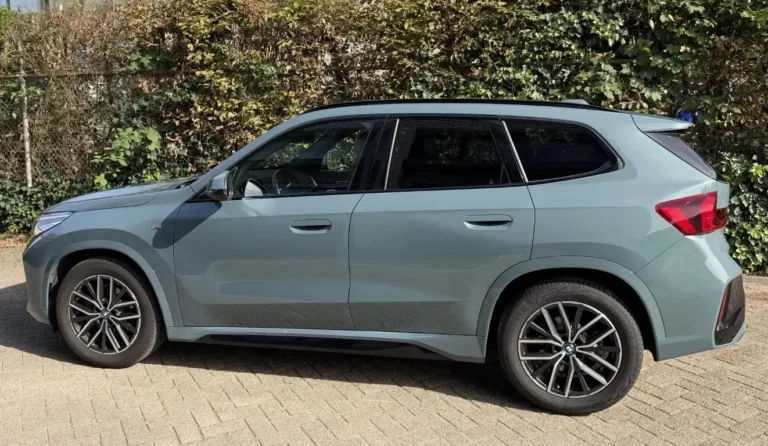 BMW iX1 occasion lease, linkerzijkant van de groene elektrische SUV met dakdraagsysteem in Shadow Line